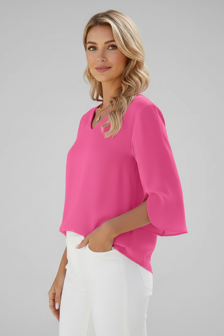 Woman in pink v-neck top with flowy sleeve detail hand on white pants pocket